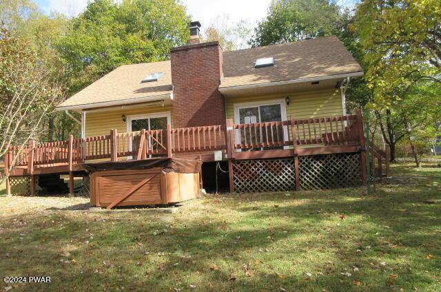 back of house with a wooden deck, a yard, and a hot tub