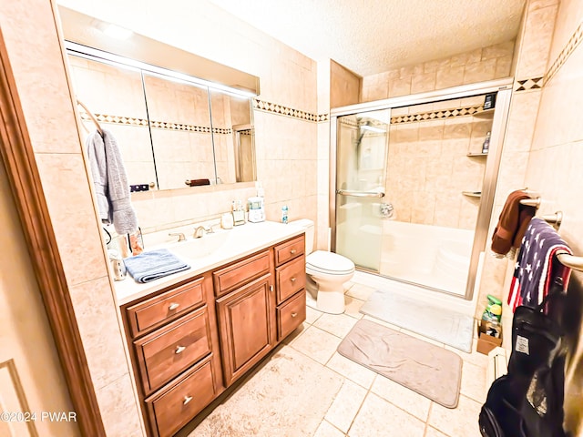 bathroom featuring a textured ceiling, toilet, a shower with door, vanity, and tile walls