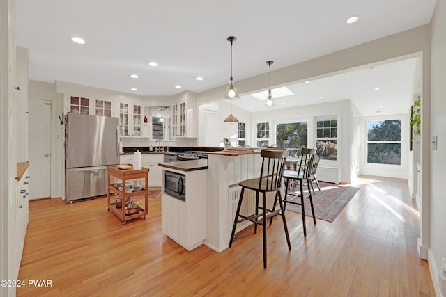 kitchen featuring white cabinetry, black microwave, stainless steel fridge, decorative light fixtures, and light wood-type flooring