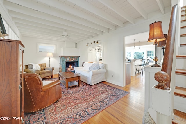 living room featuring beamed ceiling, ceiling fan, light hardwood / wood-style flooring, and a tiled fireplace