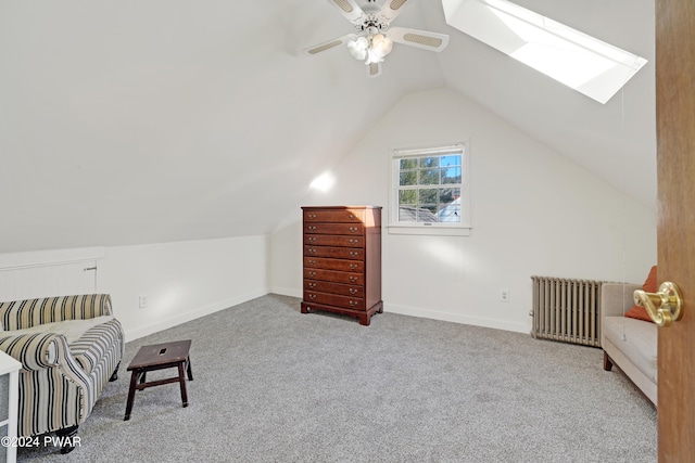 living area featuring vaulted ceiling with skylight, light colored carpet, radiator, and ceiling fan