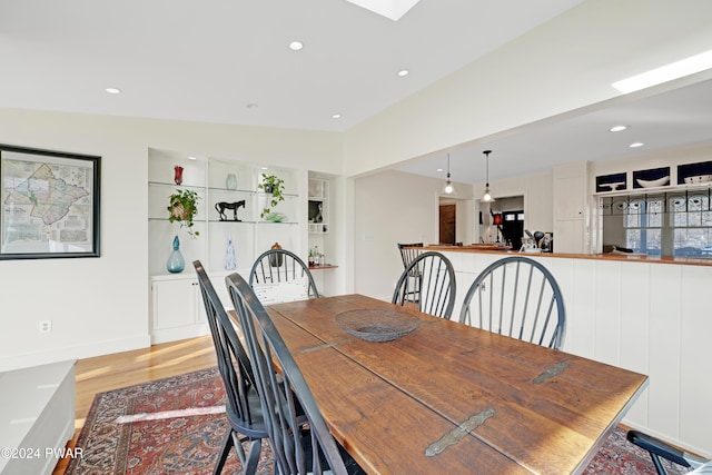 dining space featuring built in features, light hardwood / wood-style floors, and vaulted ceiling