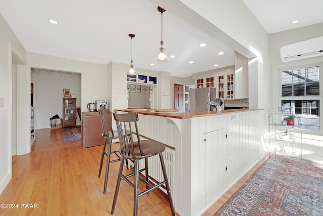 kitchen with an AC wall unit, stainless steel fridge, decorative light fixtures, a kitchen bar, and kitchen peninsula