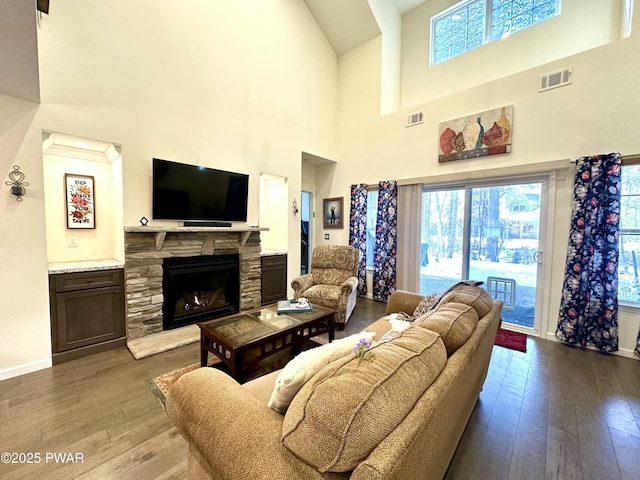 living room with a wealth of natural light, visible vents, a stone fireplace, and wood finished floors