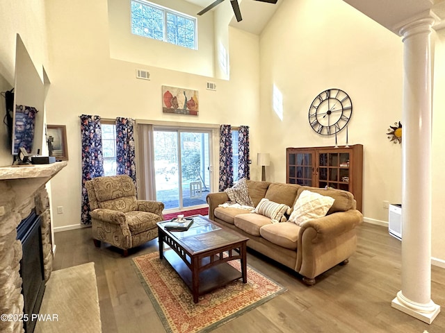 living area with decorative columns, visible vents, wood finished floors, and a stone fireplace