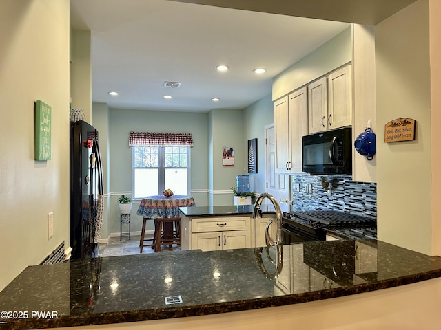 kitchen with dark stone countertops, visible vents, a peninsula, and black appliances