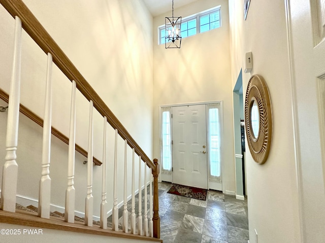 entryway featuring baseboards, a high ceiling, stairway, and a notable chandelier