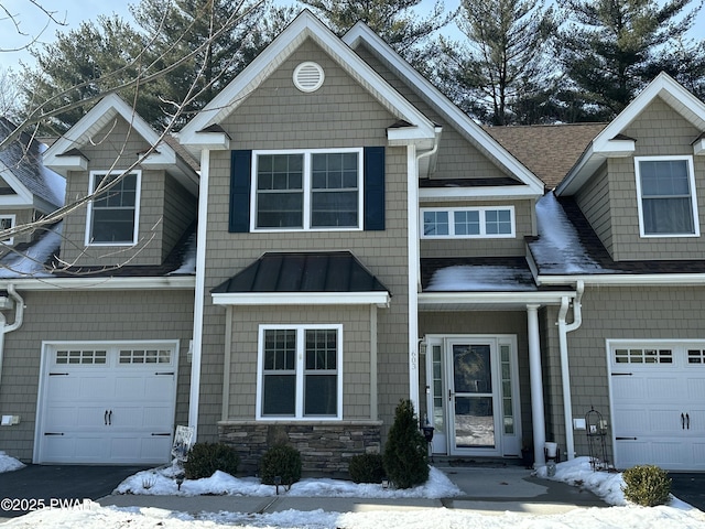 view of front facade with metal roof, aphalt driveway, a shingled roof, stone siding, and a standing seam roof