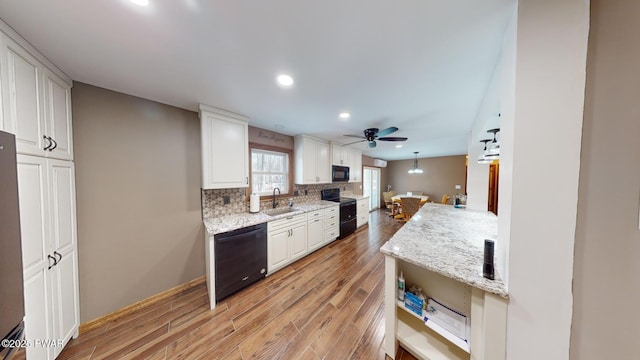 kitchen featuring tasteful backsplash, white cabinetry, sink, light stone counters, and black appliances