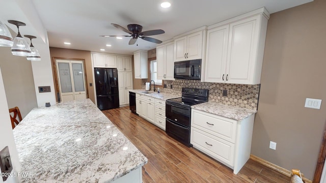 kitchen with white cabinetry, pendant lighting, light stone counters, and black appliances