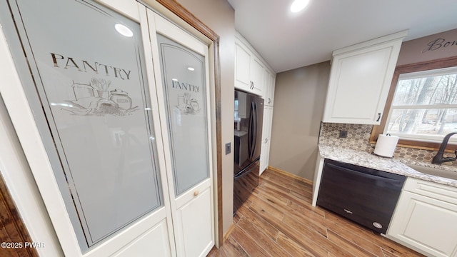 kitchen with sink, light hardwood / wood-style flooring, black appliances, light stone countertops, and white cabinets