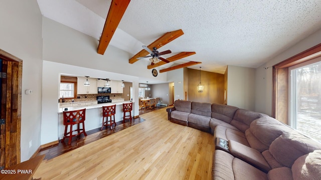 living room featuring plenty of natural light, lofted ceiling with beams, light hardwood / wood-style flooring, and a textured ceiling