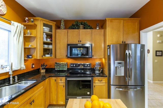 kitchen with light tile patterned floors, stainless steel appliances, dark stone countertops, and sink