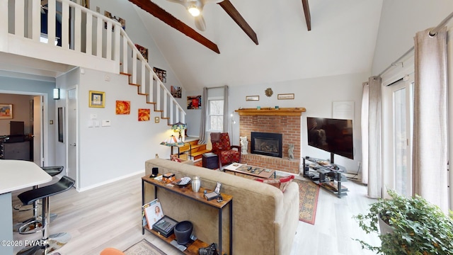 living room with a brick fireplace, high vaulted ceiling, light wood-type flooring, baseboards, and stairs