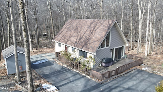 view of front of house featuring a wooded view, a shingled roof, and a wooden deck