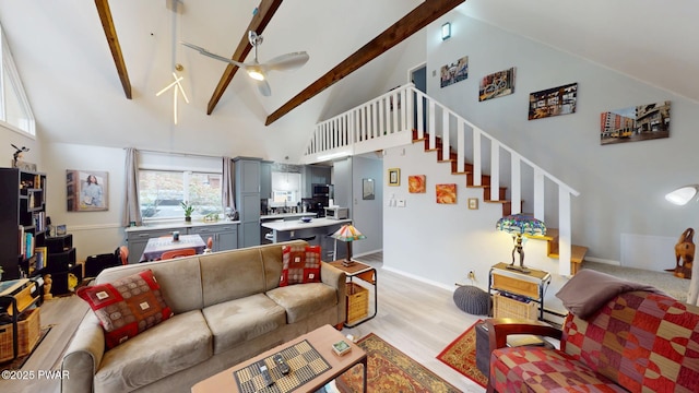 living room featuring ceiling fan, high vaulted ceiling, light wood-style floors, stairway, and beam ceiling