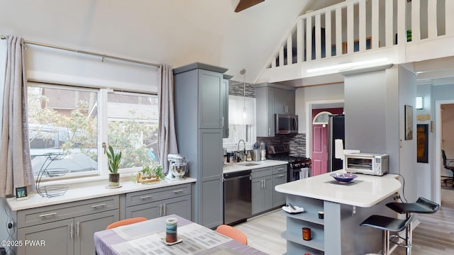 kitchen featuring a kitchen breakfast bar, a sink, stainless steel appliances, gray cabinetry, and backsplash