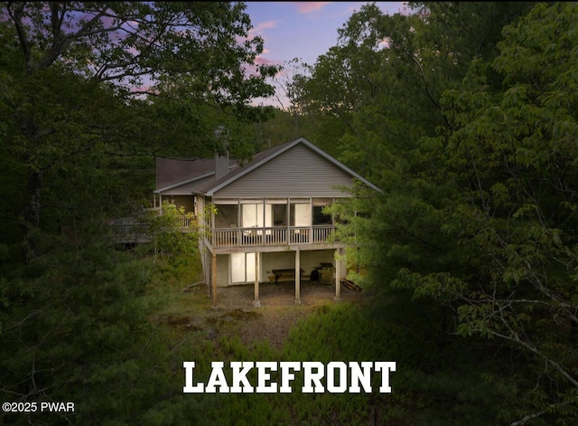 102 Circle Dr, Milford, PA 18337 - back of house at dusk with a wooden deck, a wooded view, and a sunroom