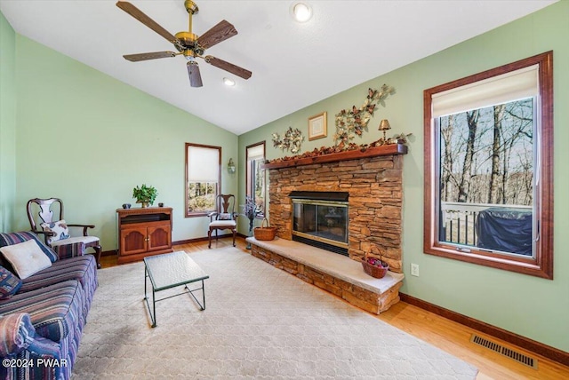 living room with ceiling fan, a stone fireplace, wood-type flooring, and vaulted ceiling