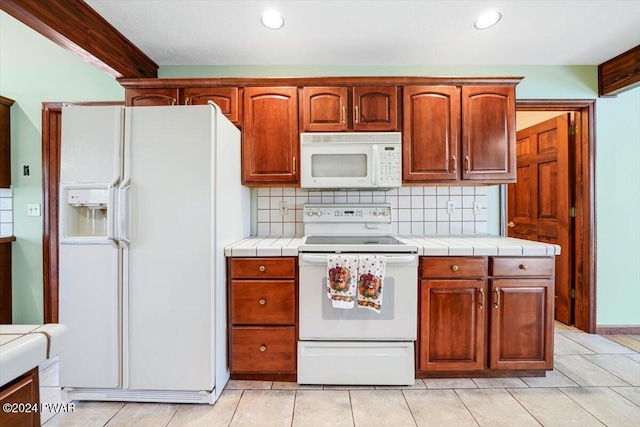 kitchen with light tile patterned flooring, white appliances, tile countertops, and backsplash