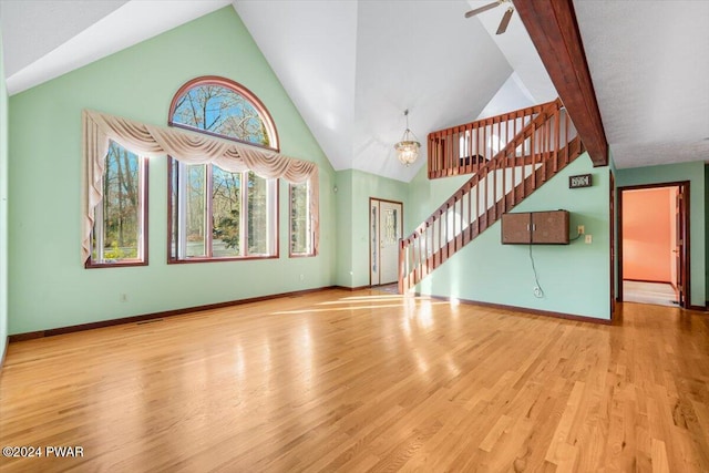 unfurnished living room featuring ceiling fan with notable chandelier, light hardwood / wood-style flooring, and vaulted ceiling