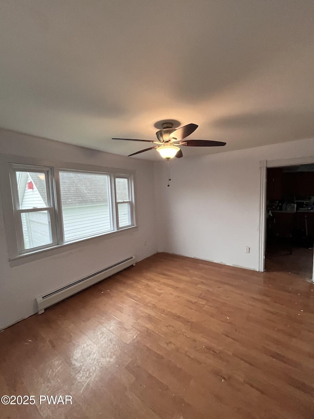 spare room featuring ceiling fan, light wood-style flooring, and a baseboard heating unit