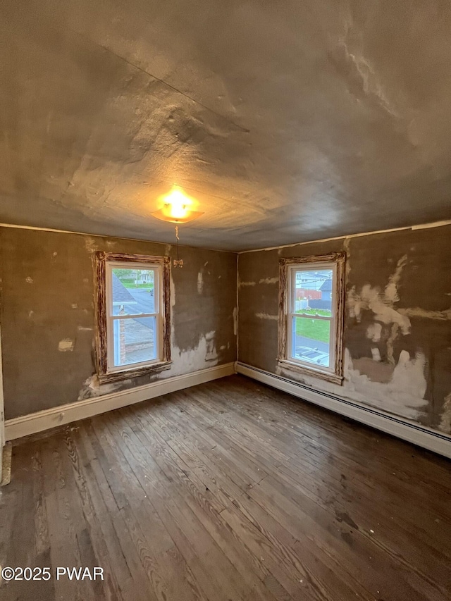 spare room featuring baseboards, a wealth of natural light, a baseboard heating unit, and hardwood / wood-style flooring