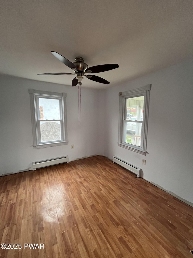 empty room with ceiling fan, wood finished floors, and a baseboard heating unit