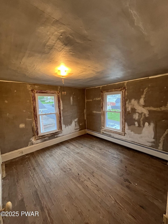 spare room featuring a healthy amount of sunlight, a baseboard heating unit, baseboards, and wood-type flooring