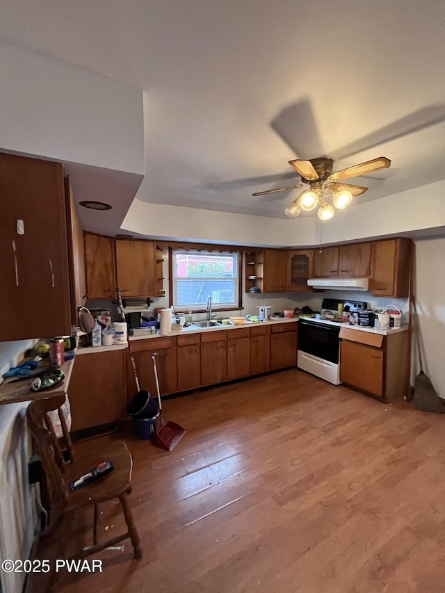 kitchen with under cabinet range hood, brown cabinets, light wood-style floors, light countertops, and electric range