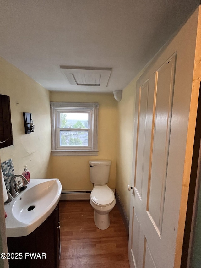 half bathroom featuring vanity, toilet, baseboard heating, and wood finished floors