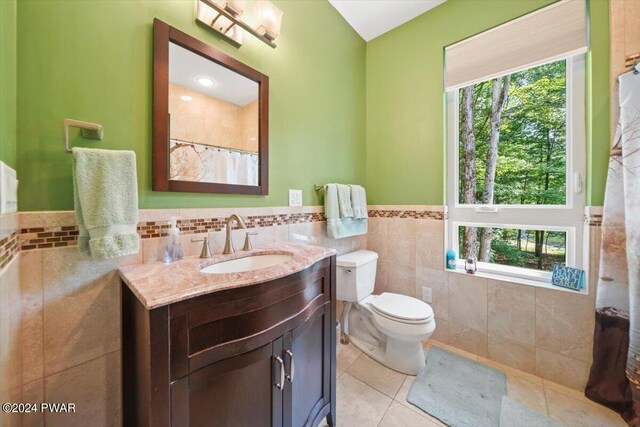 bathroom featuring tile patterned flooring, vanity, toilet, and tile walls