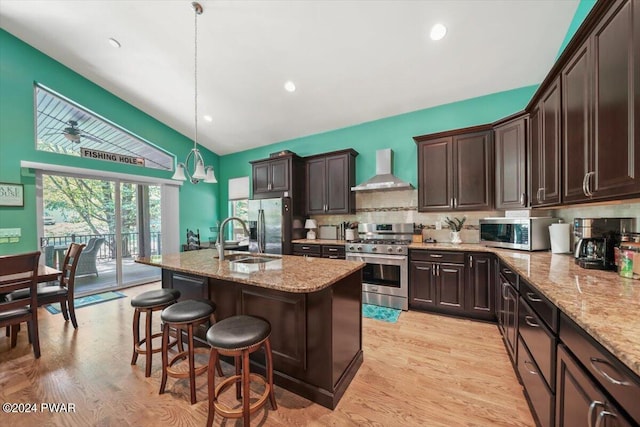 kitchen featuring appliances with stainless steel finishes, wall chimney exhaust hood, sink, pendant lighting, and a center island with sink