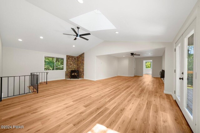 unfurnished living room featuring a fireplace, light wood-type flooring, ceiling fan, and vaulted ceiling with skylight