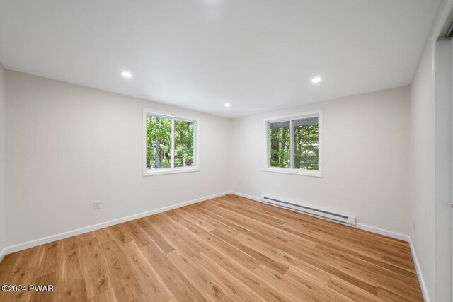 unfurnished room featuring light hardwood / wood-style floors, a wealth of natural light, and a baseboard heating unit