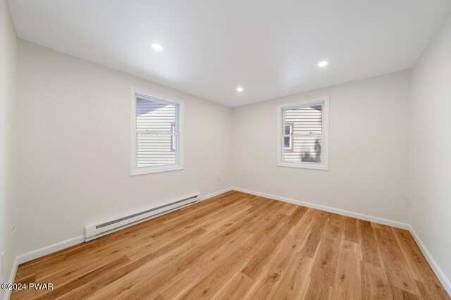 empty room with plenty of natural light, light hardwood / wood-style floors, and a baseboard heating unit