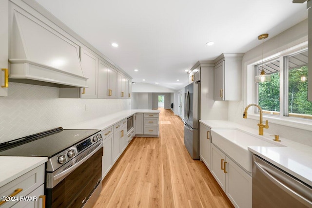 kitchen with light wood-type flooring, custom range hood, stainless steel appliances, sink, and decorative light fixtures