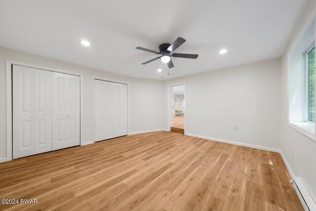 unfurnished bedroom featuring multiple windows, ceiling fan, two closets, and a baseboard heating unit