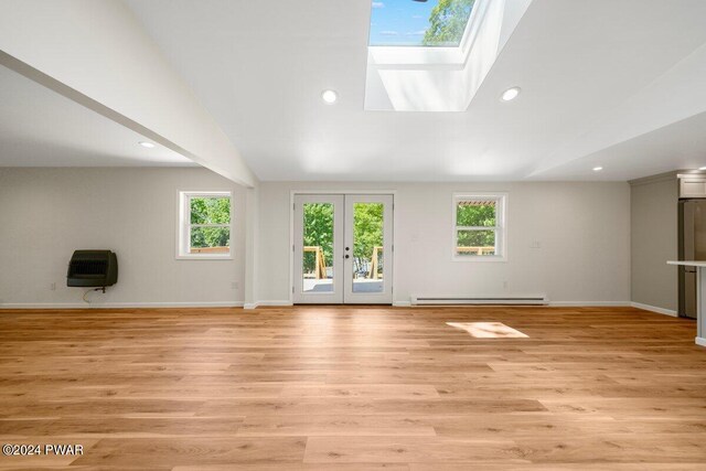 unfurnished living room featuring french doors, vaulted ceiling with skylight, a baseboard heating unit, and a healthy amount of sunlight