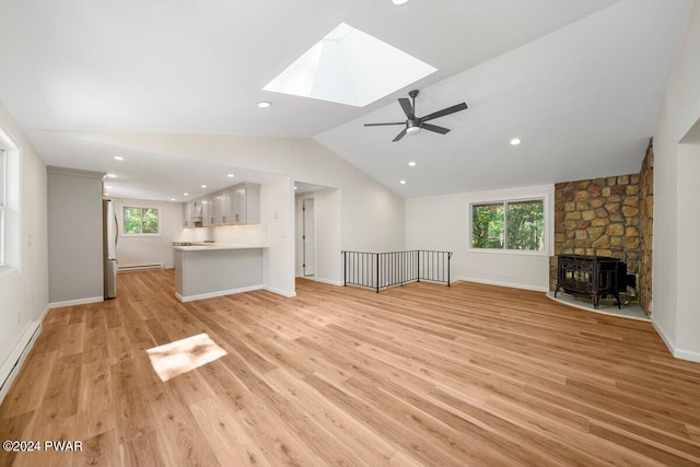 unfurnished living room with a wood stove, ceiling fan, vaulted ceiling with skylight, and a healthy amount of sunlight