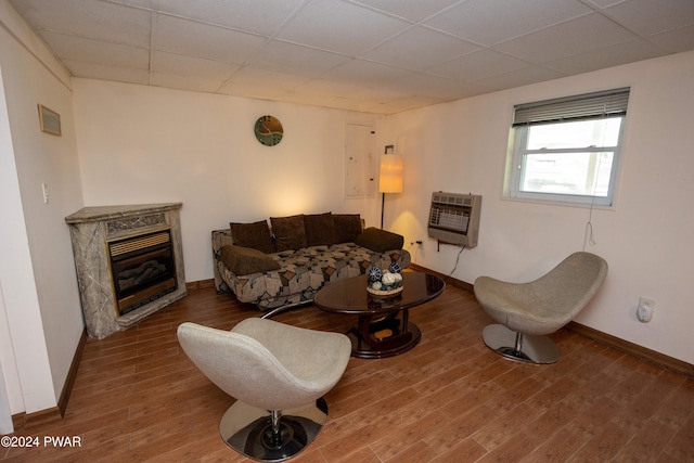 living room with a high end fireplace, a paneled ceiling, heating unit, and hardwood / wood-style flooring