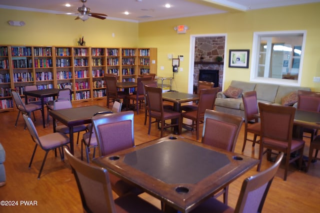 dining space with ceiling fan, a stone fireplace, crown molding, and light hardwood / wood-style flooring