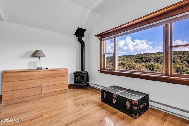 living area featuring a wood stove, lofted ceiling, light hardwood / wood-style floors, and a baseboard radiator