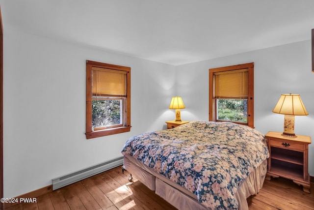 bedroom with light hardwood / wood-style floors, multiple windows, and a baseboard heating unit