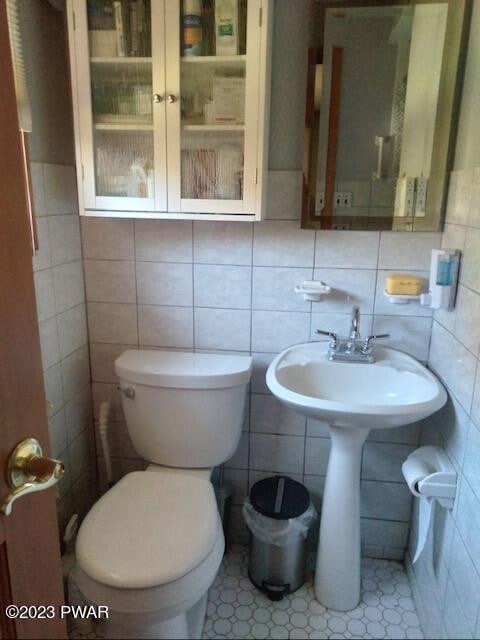 bathroom with tile patterned flooring, toilet, and tile walls