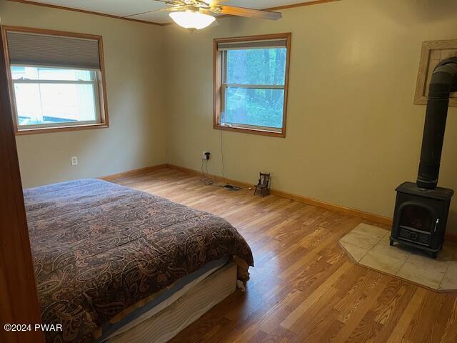 bedroom featuring a wood stove, ceiling fan, ornamental molding, and light wood-type flooring