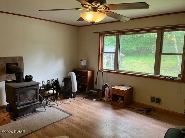 interior space featuring a wood stove, ceiling fan, light hardwood / wood-style floors, and ornamental molding