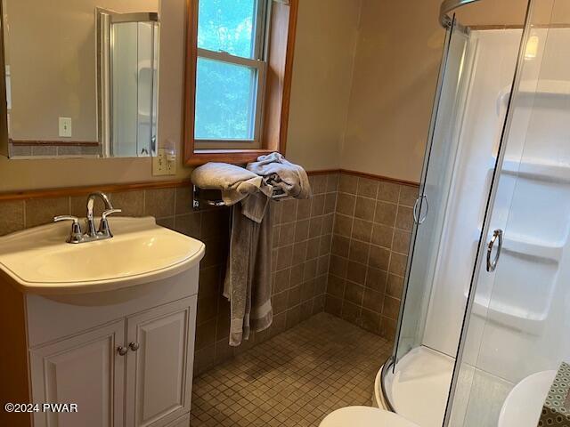 full bath featuring a wainscoted wall, a stall shower, toilet, tile walls, and vanity