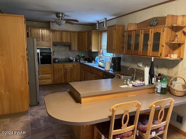 kitchen featuring kitchen peninsula, stainless steel fridge, a kitchen breakfast bar, ceiling fan, and oven