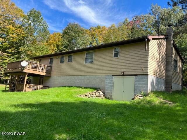 rear view of house featuring a lawn, a wooden deck, and a chimney